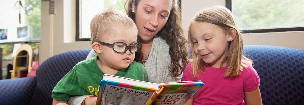 Clinical educator helping two children read a book